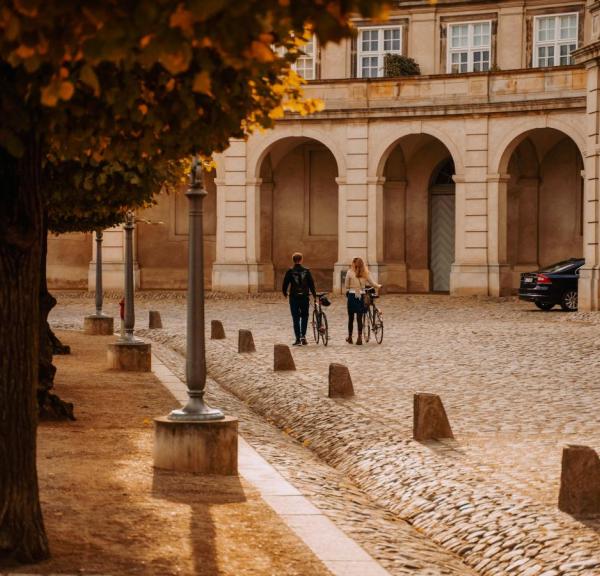 Par går med sykler over Christiansborg Slotsplads om høsten i København