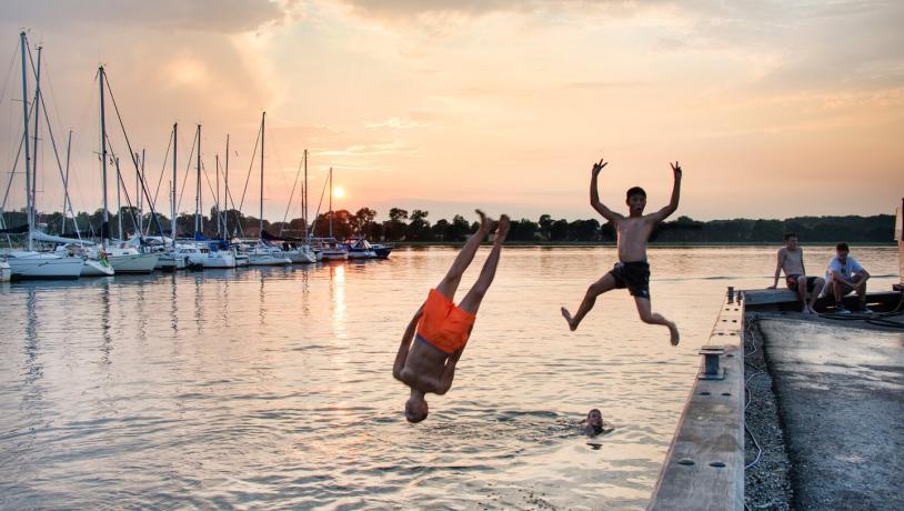 To barn hopper i vannet fra bryggen ved Præstø Havn, Sjælland, Danmark