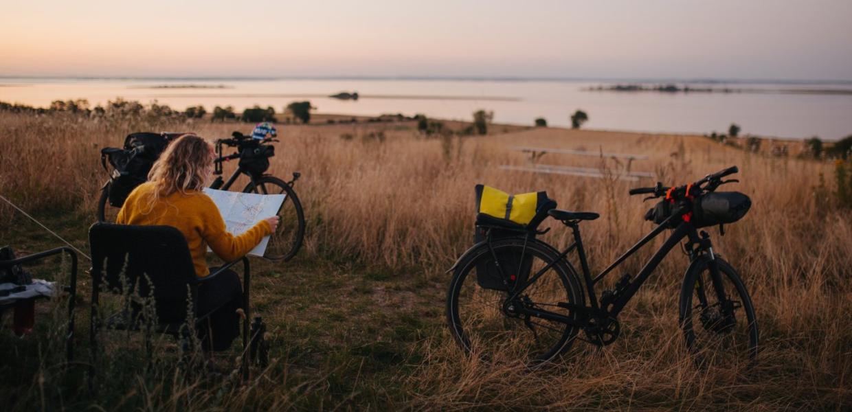 Kvinne titter på et kart mens hun sitter ved sitt telt underveis på en sykkelferie i Danmark