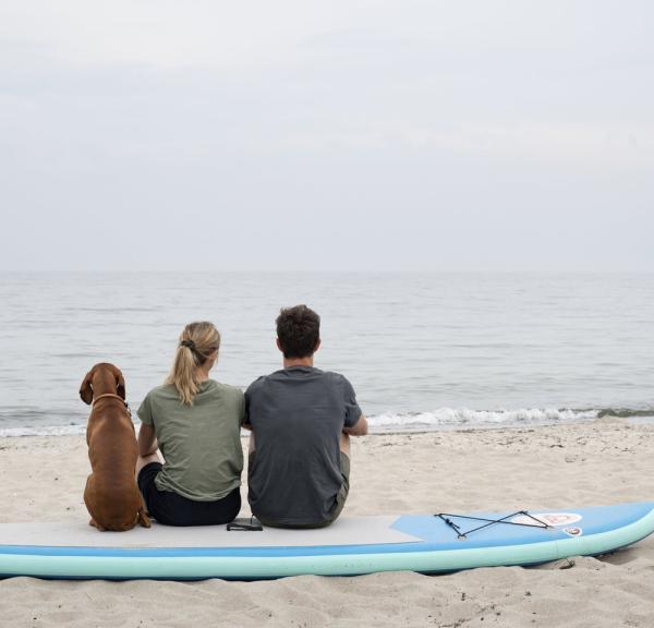Par slapper av på stranden med et paddleboard i bakgrunnen, Lolland-Falster, Danmark