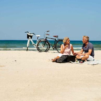 Par som har piknik på stranden i Blokhus. Sykler parkert i bakgrunnen.