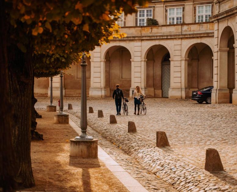Par går med sykler over Christiansborg Slotsplads om høsten i København