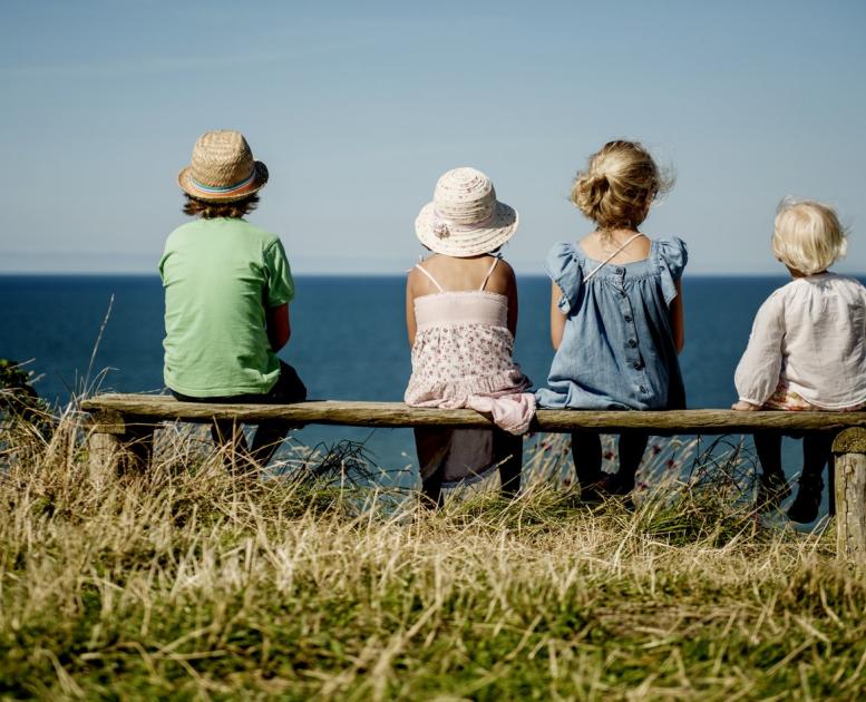 Four children sitting on a bench in Hanstholm, North Jutland, looking at the ocean.