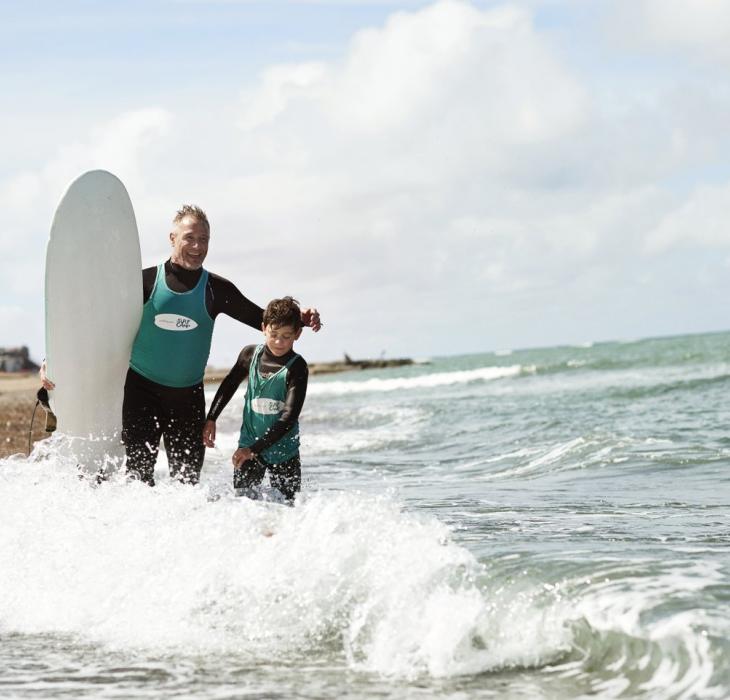 Far og sønn på vei ut i vannet for å surfe ved vestkysten, vestjylland, Danmark